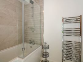 A bathroom with a bathtub shower, glass shower screen, wall-mounted showerhead, and a chrome heated towel rail at Yr Hen Dy Capel in Blaenau Ffestiniog