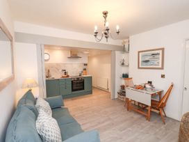 A living area with a blue sofa and a small dining table with two wooden chairs next to an open kitchen with green cabinets at The Riddle in Whitby