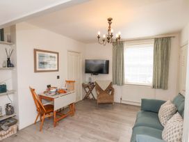 A living room with a dining table and chairs a sofa with cushions a wicker chair a wall mounted TV and a window with curtains at The Riddle in Whitby