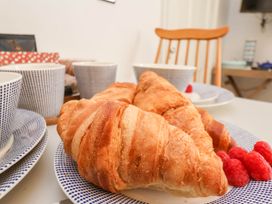 A table setting with croissants, raspberries, cups, and plates with a wooden chair in the background at The Riddle in Whitby