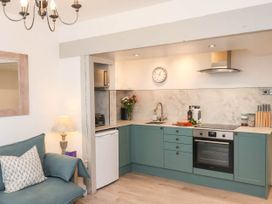 A kitchen with green cabinets, a stove, oven, sink, and a living area with a blue sofa and a lamp at The Riddle in Whitby