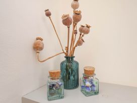 A blue glass vase with dried seed pods and two small glass jars with cork lids containing marbles on a white surface at The Riddle in Whitby