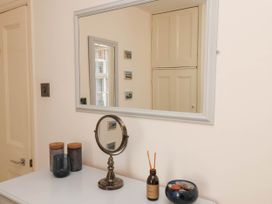A dresser with jars, a round mirror, an aroma diffuser, and a small bowl in a room with a mirror on the wall at The Riddle in Whitby