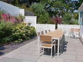 An outdoor patio with a long dining table and chairs next to a white picket fence and garden at Argraig in Llanbedrog