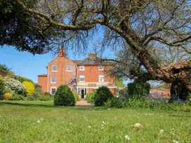 A large brick house with multiple windows and a garden with bushes flowers and a large tree at Hilltop House in Tenbury Wells