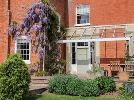 A garden patio with a climbing purple flower plant on a brick house with wooden chairs at Hilltop House in Tenbury Wells