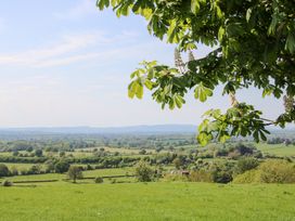 A countryside landscape with green fields trees and hills under a blue sky with tree branches in the foreground at Hilltop House in Tenbury Wells
