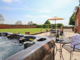 An outdoor patio with a hot tub a table with champagne bottles and glasses and a seating area with umbrella at The Chestnuts in Tenbury Wells