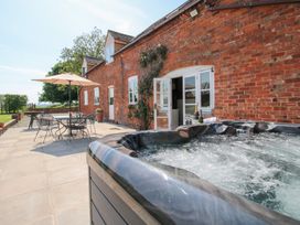 An outdoor patio with a hot tub a table and chairs with an umbrella and a brick building in the background at The Chestnuts in Tenbury Wells