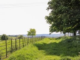 A grassy path with metal fencing on the left and trees on the right with hills in the background at The Chestnuts in Tenbury Wells