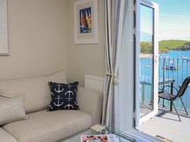 A living room corner with a beige sofa and anchor print cushions next to an open balcony door overlooking water and boats at 37 The Salcombe in Salcombe