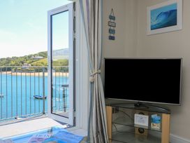 A corner of a room with a television on a stand and an open door leading to a balcony overlooking water at 37 The Salcombe in Salcombe