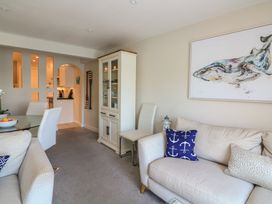 A living room with a glass dining table and chairs a white cabinet and a sofa with cushions with a painting of a whale above at 37 The Salcombe in Salcombe