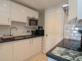 A kitchen with white cabinets a stainless steel sink a microwave a kettle a toaster and a hob at 37 The Salcombe in Salcombe