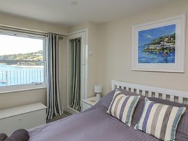A bedroom with a bed with striped pillows a bedside table with a lamp a framed painting and a window with a view of the sea at 37 The Salcombe in Salcombe