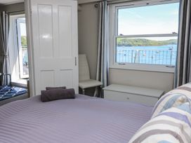 A bedroom with a bed covered in a purple striped blanket and two purple towels on it a white chair a white chest a window with curtains showing a view of water boats and green hills and an open door leading to another room with a blue patterned rug at 37 The Salcombe in Salcombe