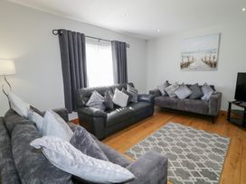 A living room with three sofas a patterned rug a lamp curtains and a wall painting at SeaShells in Castlerock