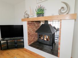 A room with a wood burning stove in a brick fireplace and a television on a black stand at SeaShells in Castlerock