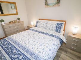 A bedroom with a bed with floral bedding a bedside table with a lamp and a chest of drawers with decorative items at SeaShells in Castlerock