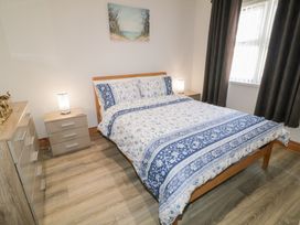 A bedroom with a bed with patterned bedding two bedside tables with lamps a dresser and a window with curtains at SeaShells in Castlerock