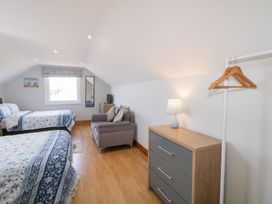 A bedroom with two beds a grey armchair a chest of drawers with a lamp a standing rack with hangers and a window with a blind at SeaShells in Castlerock