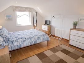 A bedroom with a wooden bed with blue patterned bedding a window a small TV on a chest of drawers a clothes rack and a larger dresser in SeaShells Castlerock
