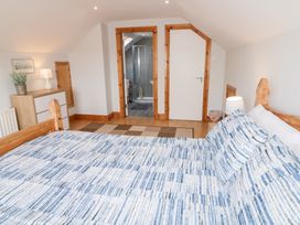 A bedroom with a bed covered in a blue and white patterned bedspread a chest of drawers with a lamp and plant and a door leading to a bathroom at SeaShells in Castlerock