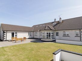 An exterior view of a white house with tiled roof a lawn and wooden benches on a patio at SeaShells in Castlerock