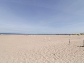 A sandy beach with white posts leading to the sea and a few people near sand dunes at SeaShells in Castlerock