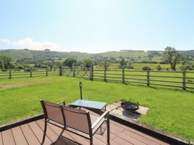 A patio with a chair and table overlooking a grassy field at Bwthyn Bach Brefi