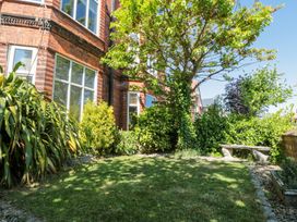 A garden with grass trees bushes a stone bench and a brick house in the background at Royal Victoria House in Scarborough