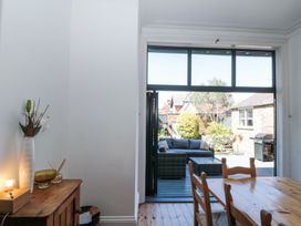 A dining area with wooden chairs and table next to a wooden cabinet with a vase and lamp opening to an outdoor patio with seating at Royal Victoria House in Scarborough