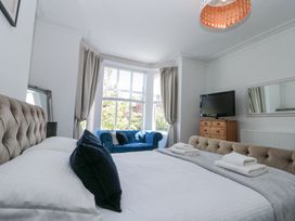A bedroom with a large bed with pillows and folded towels a blue sofa in front of a bay window a wooden dresser with a TV and a large wall mirror at Royal Victoria House in Scarborough