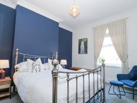 A bedroom with a metal bed frame blue accent wall bedside tables with lamps blue armchair and white curtains at Royal Victoria House in Scarborough