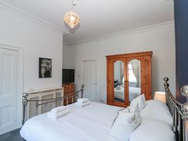 A bedroom with a metal bed frame white bedding wooden wardrobe with mirrors and a chest of drawers with a television at Royal Victoria House in Scarborough