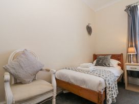 A bedroom with a wooden bed, a white armchair with a cushion, a bedside table with a lamp, and a window with curtains at Royal Victoria House in Scarborough