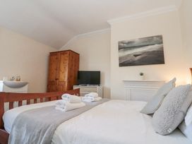 A bedroom with a bed and gray pillows folded towels a wooden wardrobe a sink a tv and a painting above a white fireplace at Royal Victoria House in Scarborough