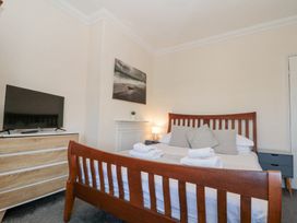 A bedroom with a wooden bed frame, folded towels on the bed, a dresser with a TV on it, a bedside table with a lamp, and a wall picture at Royal Victoria House in Scarborough