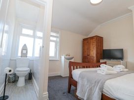 A bedroom with a wooden bed with towels on it, a wooden wardrobe, a TV on a white cabinet, and an adjacent small toilet with a window at Royal Victoria House in Scarborough