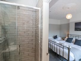 A bathroom shower with glass door and tiled walls next to a bedroom with a double bed and a single bed at Royal Victoria House in Scarborough
