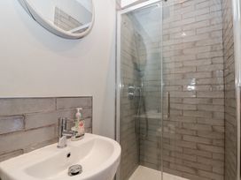 A bathroom with a white sink and a chrome faucet next to a glass shower enclosure with grey tiled walls at Royal Victoria House in Scarborough
