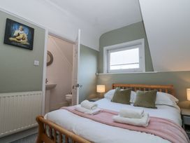 A bedroom with a wooden bed two green pillows two bedside tables with lamps an open door to a bathroom and a window with blinds at Royal Victoria House in Scarborough