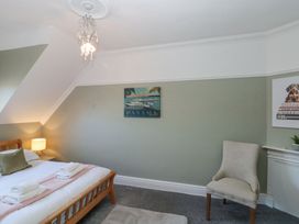 A bedroom with a wooden bed a bedside table with lamp a beige chair and wall art at Royal Victoria House Scarborough