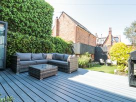 An outdoor patio with a wicker sectional sofa and glass coffee table adjacent to a garden with chairs and greenery at Royal Victoria House in Scarborough