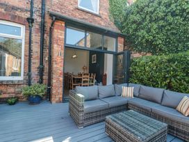 An outdoor patio area with wicker seating and cushions next to a brick building with an open door showing a dining area inside at Royal Victoria House in Scarborough