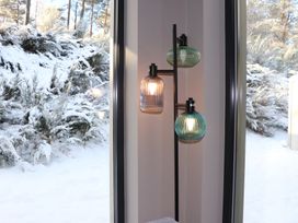 A lamp near a window with snow and trees outside at Wildcat Lodge in Feshiebridge near Aviemore