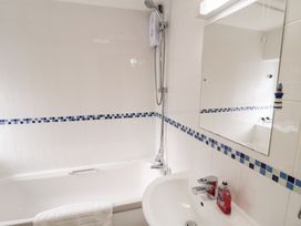 A bathroom with a bathtub, shower, and sink at Cobbler's Cottage Mundesley
