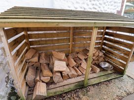A wood storage shed filled with firewood and a metal bowl at Cobbler's Cottage Mundesley