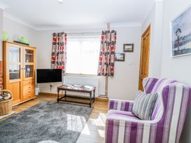 A living room with a striped purple armchair a wooden cabinet a mounted television and a coffee table near a window with patterned curtains at Lillies Pad in Methwold near Feltwell
