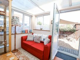 A conservatory with a red sofa and cushions beside glass display and open door to garden at Lillies Pad in Methwold near Feltwell